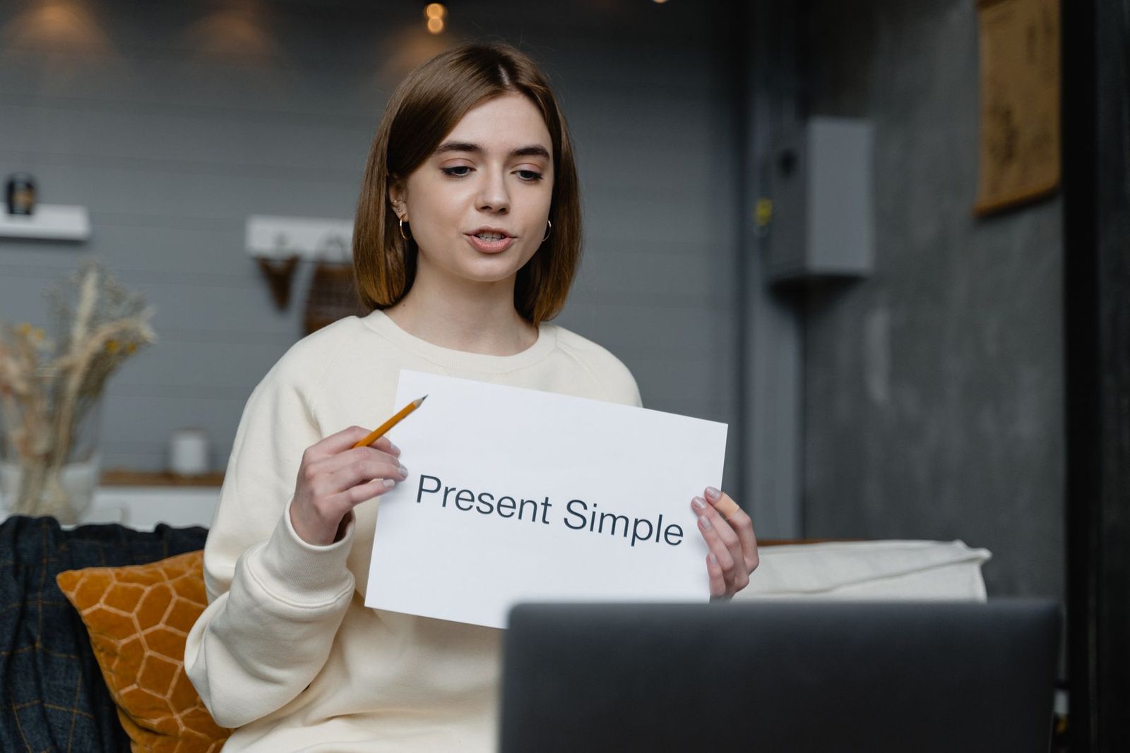Lehrerin erklärt online englische Grammatik und hält einen Zettel mit „Present Simple“